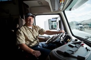 Truck driver (30s) sitting in cab of semi-truck.